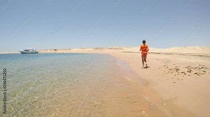 Little girl in swimwear running away on the sea beach in desert