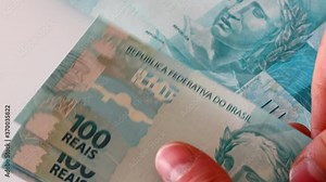 Brazilian money, 100 Real banknotes held in the hand and placed individually on the table, A large amount of currency