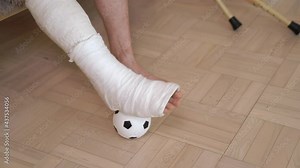 Guy with a broken right leg exercising a leg with a soccer ball