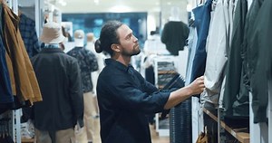 rational shopping man being more mindful of his purchases, choosing things he needs with his values, such sustainability quality. standing in store, man chooses autumn clothes rational shopping