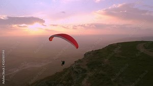 Professional paraglider float in air on parachute. Man paragliding and descending down from sky in beautiful pink sunset. Amazing adventure or activity to try new experiences