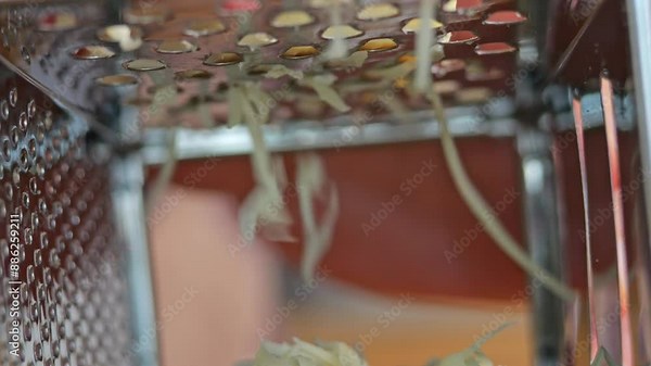 Grating cheese for pizza in slow-motion macro view. A man's hand uses the grater, shredding cheese. Detailed look at the grater, blades, and cheese shreds.