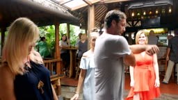 Man dancing with a group of women takes his shirt off in a bar while...