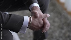 Close-up of a man's hands clasped together, wearing a suit and a silver bracelet.