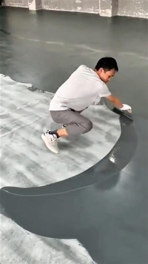 applying a layer of gray epoxy resin to a concrete floor surface using a squeegee tool indoors