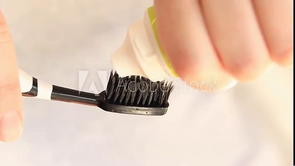 Squeezing toothpaste onto a toothbrush, close-up. Brushing your teeth. Healthcare, oral hygiene. A woman squeezes white toothpaste from a tube onto a black toothbrush. Morning hygiene procedures