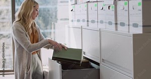 Wide shot of a woman unpacking files out of boxes and into a filing cabinet