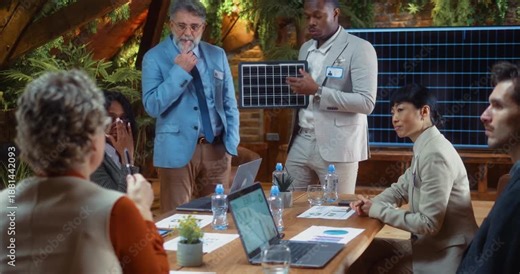 Black businessman presents solar panel model to team, explaining renewable energy solution and clean technology system during professional meeting in modern eco office.