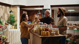 Senior vendor assisting clients in eco friendly shop with ethical sourced organic food items, providing recommendations. Couple in local store chatting with trader about pantry staples bulk products