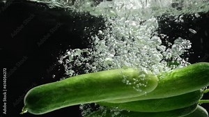 A Cucumber (Cucumis sativus) falling into the transparent water on black background and making air bubbles. Food commercial concept
