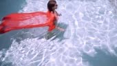 female in a pink long dress swims in a blue pool under water. Pink...
