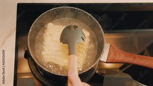 POV hands cooking instant noodle soup at home. Female hand used heat-resistant silicone cookware shifting noodles with a spoon into from pan to bowl at home. Steaming food on gas stove.