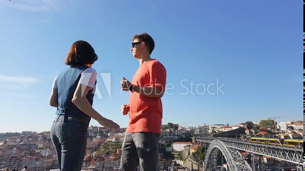 Tourists dancing on a wall and contemplating the beautiful view of the old town with river and iron bridge in the city of Porto, Portugal. Enjoying the vacations.