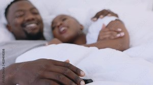 Bedroom, movies and love couple watching TV at night talking or decide on channel in their home or on the weekend. Happy woman or black people hugging or cuddle in bed with romantic television film