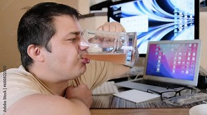 A man greedily drinks a big glass mug with cold beer and puts it on the desktop with a computer monitor and a tablet.