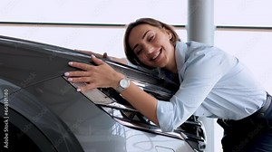 Beautiful woman hugging a new car in a car showroom
