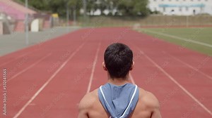 View from back of a pumped-up man standing on the running lane of stadium and looking forward, slide up. Muscular athlete looks to stadium, a view from the back. Concept moving forward