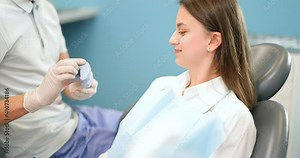 Dentist showing a jaw model, explaining to the young patient the process of orthodontic treatment. Girl with dental braces with a dentist