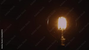 Incandescent light bulb isolated on black background. Glass and metal base. Lights up brightly with blinking and fades out. Edison lamp. 4K resolution