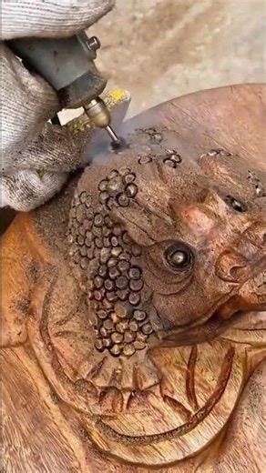 carving detailed skin patterns on a wooden frog sculpture using a small electric rotary tool indoors