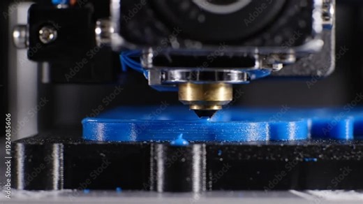 Close up view of a 3D printer nozzle extruding blue plastic filament to create a layer