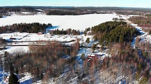 Descending drone footage flying towards an empty camping site covered in snow on a beautiful sunny winter day. In the background there is a frozen lake also covered in snow. Filmed in realtime at 4k.