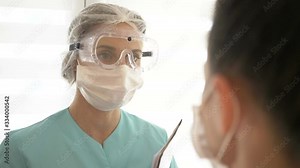 Nurse in a medical mask and glasses measures the patient's temperature with a non-contact infrared thermometer.
