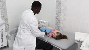 a little girl at a pediatric checkup with her doctor. An African-American doctor examines the internal organs of the abdominal cavity of a child