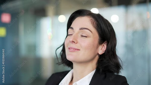 Businesswoman in formal attire taking a moment to relax with closed eyes in an office environment. A happy female feels relaxation, mindfulness, peace. Close-up of a woman practicing stress relief.