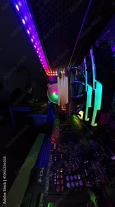 Vertical video. Zoom out. A man finishes working at his desk and places his legs on the table, captured in a wide-angle, close-up view from inside a gaming PC, highlighting the vibrant RGB lighting an