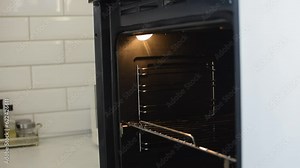 A woman opens the oven door and puts a container of food in the oven