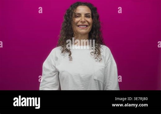 Hispanic young woman smiles and holds up hand in peace sign gesture against vibrant pink studio wall; peace Stock Video Footage - Alamy