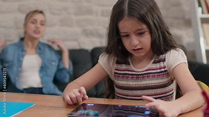 Young mother yells at her daughter who does not do her homework and is constantly playing games on the tablet computer.The little girl gets angry and covers her ears with her palms.Computer addiction.