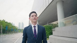 Shot of business working man walking along city walking path near glass office building with business briefcase, smart formal outfit, urban commuter walking along sidewalk, stop at look at the watch