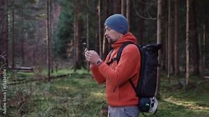 Hiker use smartphone for navigation in woods during autumn outdoor hiking expedition. Traveler using GPS navigational application on phone along walking through forest. Geographic Positioning System.