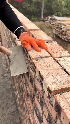 building a brick wall by laying mortar and placing red bricks in a straight line for construction