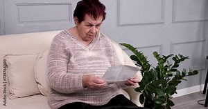 Angry stressed elderly old woman 80s, opening envelope reading bad news and tears up mail letter. Mad female feels frustrated by high bills, bank debt, tax invoice or mistake.