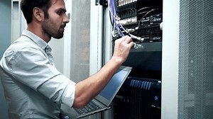 IT Engineer Patching Network Equipment In Server Room. Network Engineer Maintenance Work In Server Room . IT Technician Works With Ware And Cables in Big Data Center. Connecting Lan Cable To Mainframe