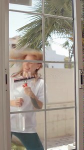 girl dances while washing windows,combining everyday activities with lively movement. Her light-hearted demeanor gestures lighten the mood, creating atmosphere and fun in the cleaning process.Vertical