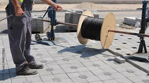 Unwinding cable of spool, coil at construction site Cable spool is on the axle until worker unwinds wire at building site.