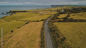 Aerial autumn road: car travel view. Beautiful Northern Ireland countryside nature scene with roadway against Atlantic cliffy shoreline in yellow fall tones. Footage shot in 4K, UHD