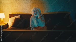 Happy old woman watching a night comedy show on TV and laughing, sitting on sofa