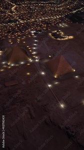 Aerial top view of the Pyramids of Giza at dusk in Egypt. The city and the pyramids illuminated