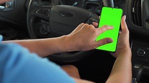 Female driver using a smartphone inside the car. Chromakey smartphone with green screen. Auto navigation. Internet addiction. Automobile insurance application.