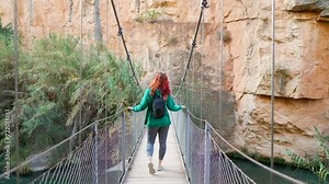 rear view of woman walking relaxed on wooden suspension bridge with beautiful cliff view
