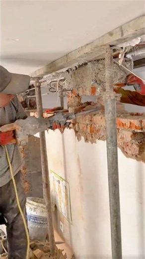 Construction worker using demolition hammer to break concrete wall