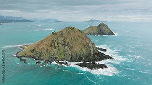 Beautiful teal blue waters around island in Pacific Ocean. Hawaii tourism concept, Kailua on background. Drone flying above Na Mokulua island on cloudy summer day. Scenic tropical island landscape
