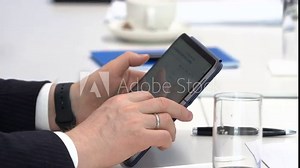 Hands holding tablet. Hand scrolls screen with finger. White table, glass, pens unfocused on background