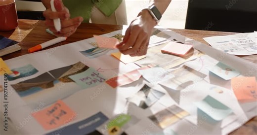 Designer reacting to storyboard unrolling is placing orange sticky notes to map workflow on table