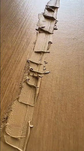 Applying wood filler to a gap in a wooden surface then smoothing it out using a metal putty scraper